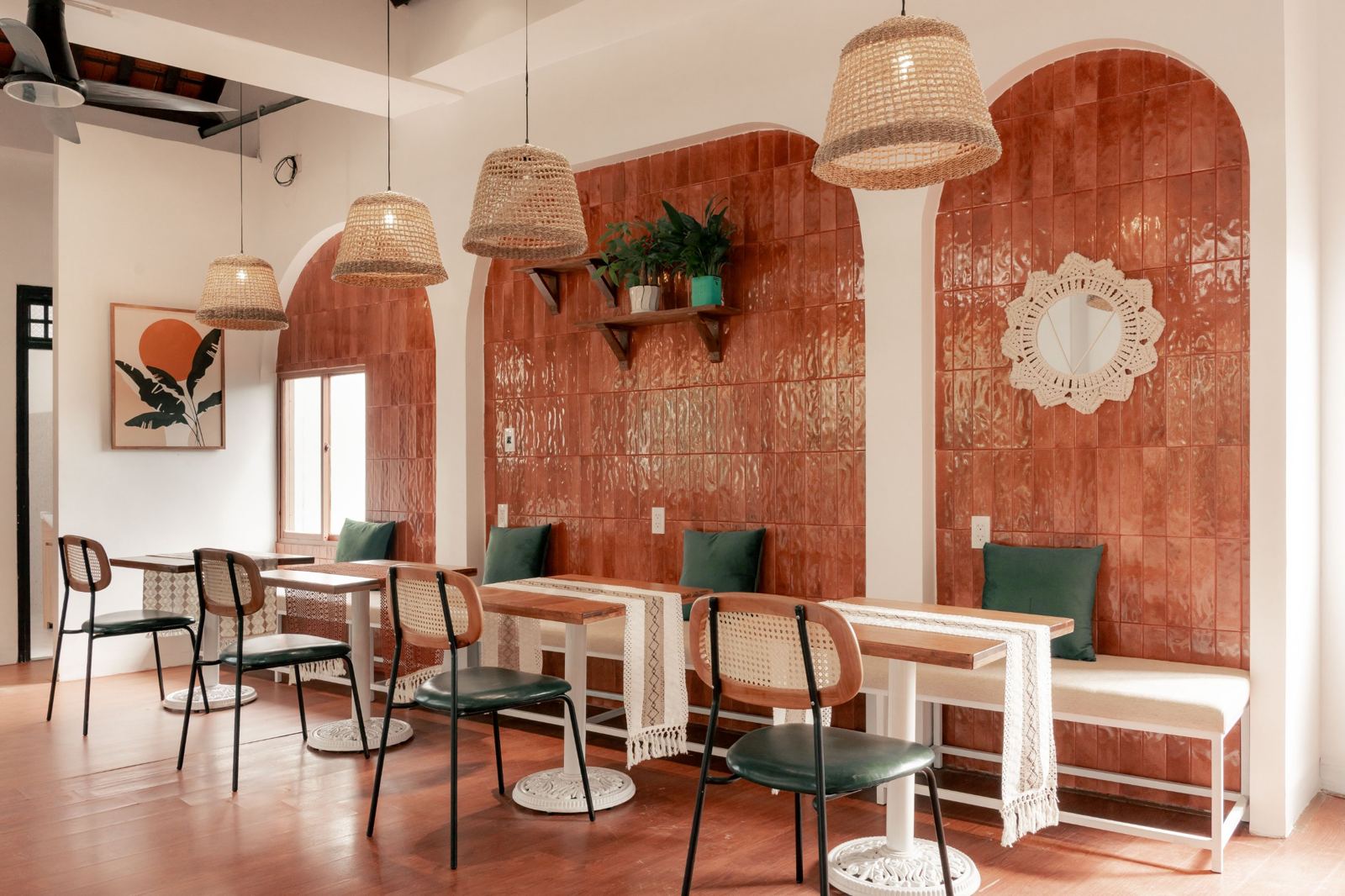 Indoor room with terracotta tiled arches, bench seating with green cushions and woven lamps