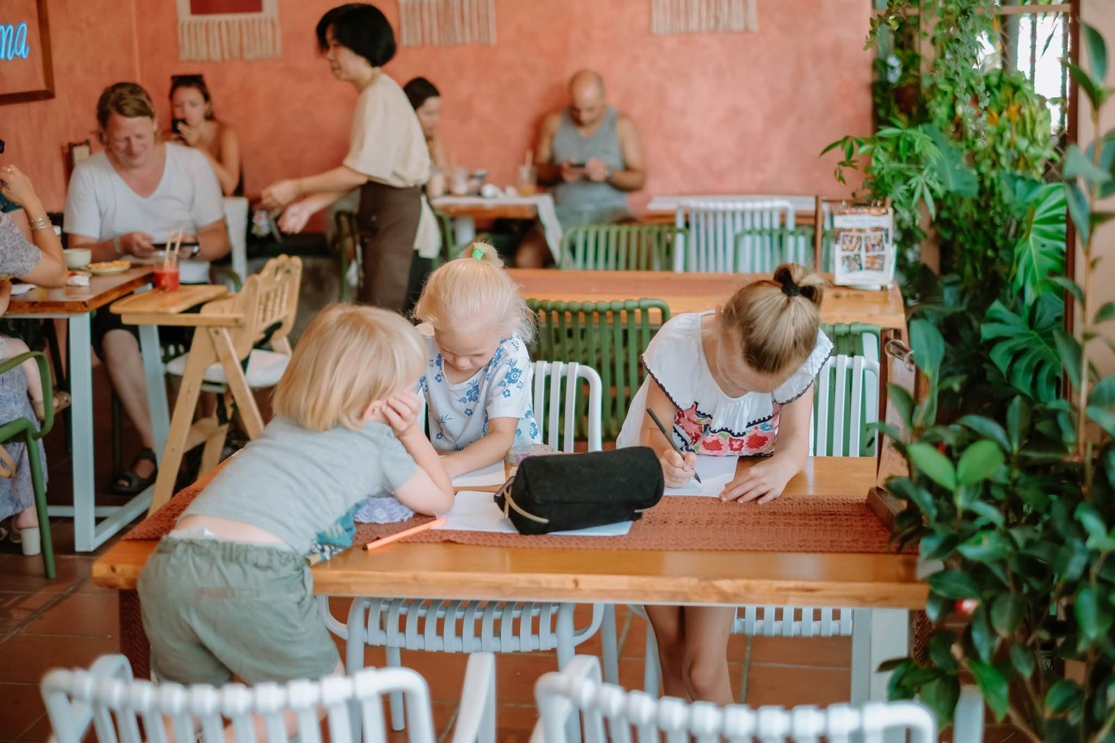 Three children drawing at a terrace table while parents have brunch