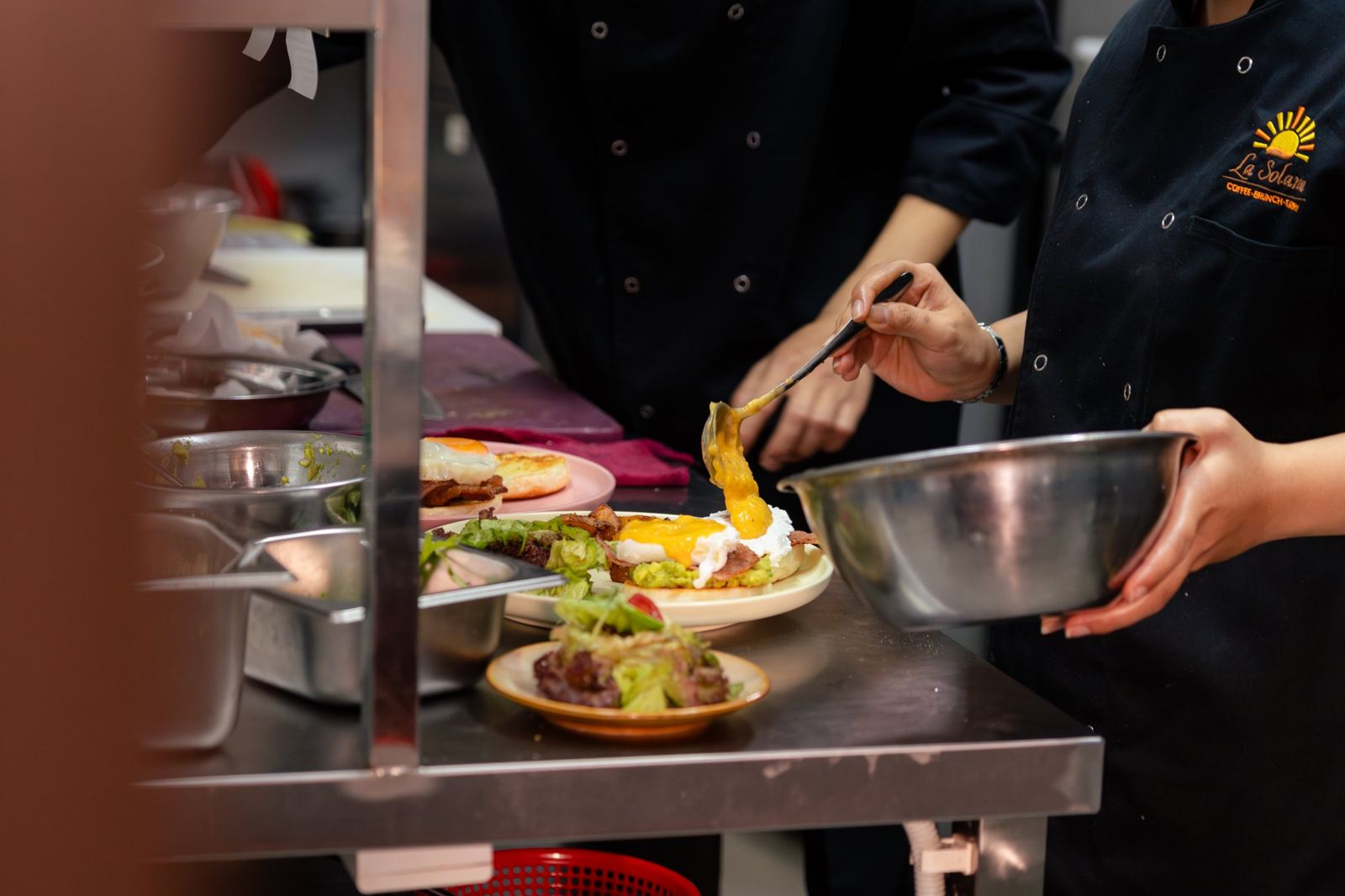 A cook spooning hollandaise over Eggs Benedict in La Solana's kitchen
