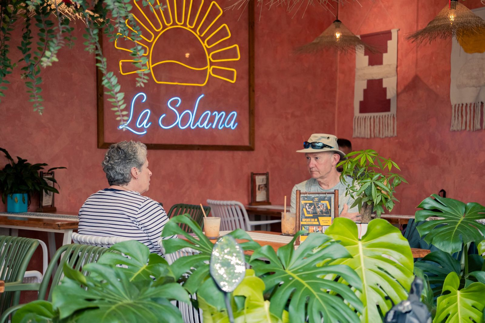 Two guests talking over iced coffee under the La Solana neon sign