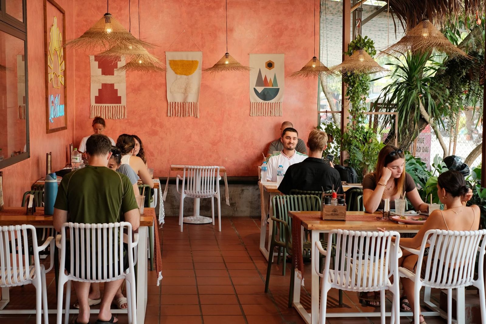 Guests at lunch on the ground-floor terrace, with woven wall hangings and the neon sun sign