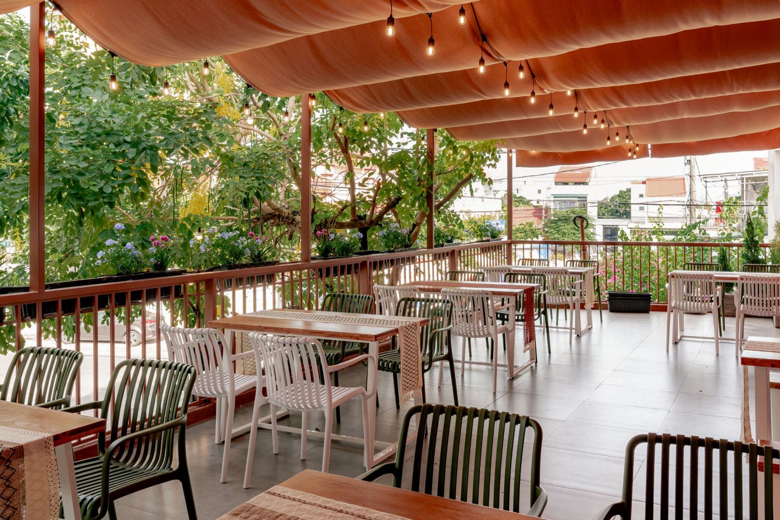 Upstairs terrace under a peach canvas canopy and string lights, with trees and flower boxes along the railing